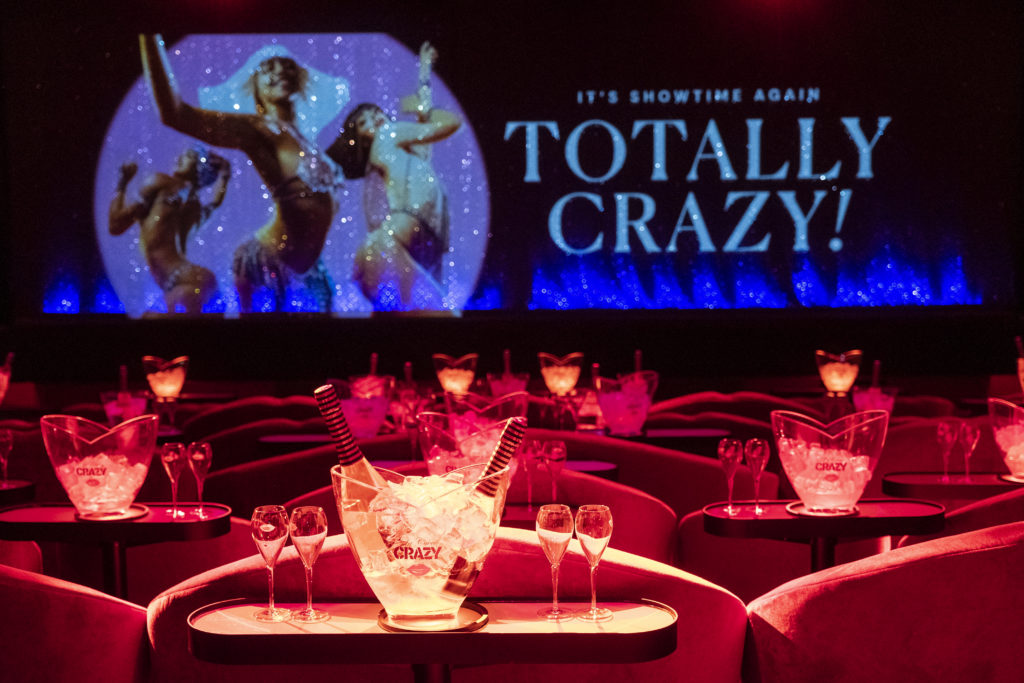 Organiser un événement d'entreprise à Paris - salle du Crazy Horse - champagne et coupe de champagne au premier plan, rideau avec projection Totally Crazy en arrière plan