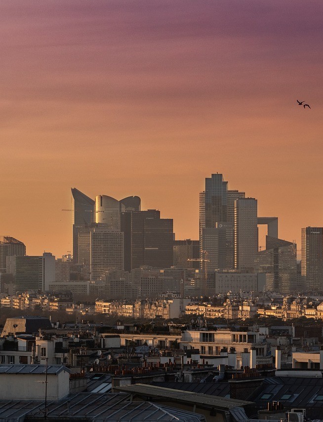 Organiser un évènement d'entreprise à Paris - les toits parisiens en premier plan, le quartier de la Défense au coucher du soleil en arrière plan