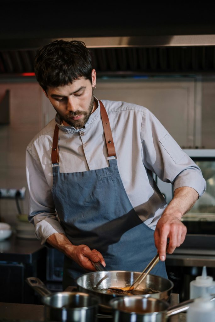 Organiser un évènement d'entreprise à Paris - un homme avec un tablier bleu cuisine dans un une cuisine de restaurant 